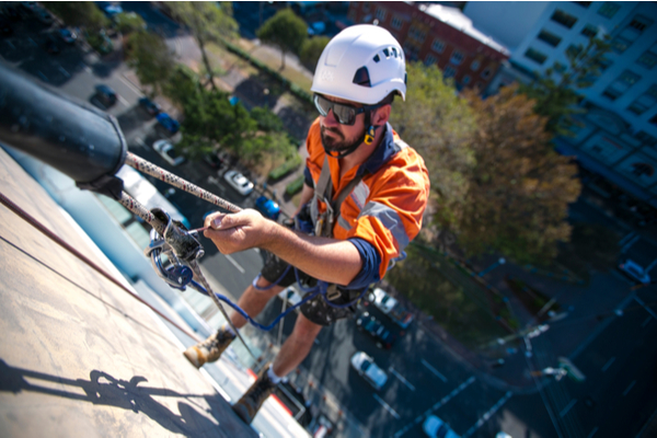Man wearing a hardhat and harness using a rope on a construction building