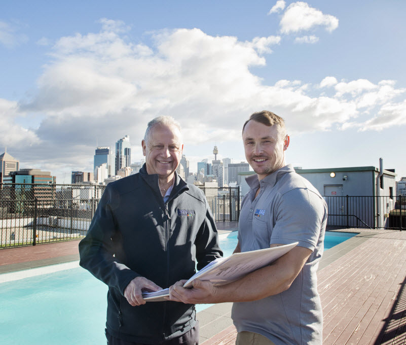 Two men checking a design while on the roof with a pool