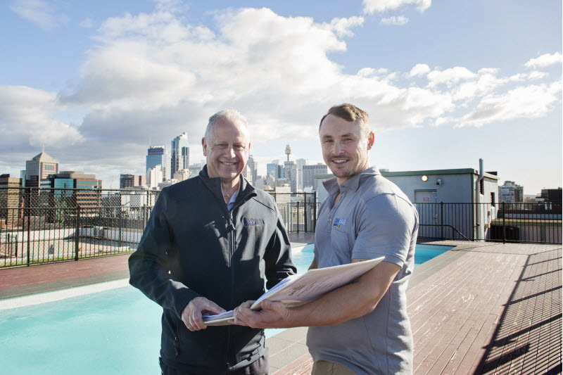 Two men checking a design while on the roof with a pool