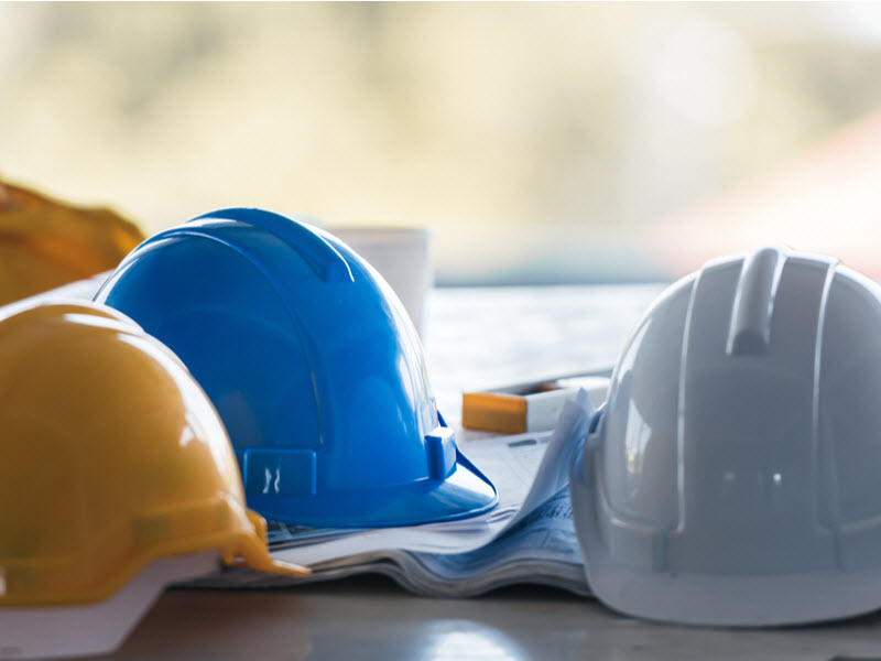 Three different colours of hard hat on the table with blueprint