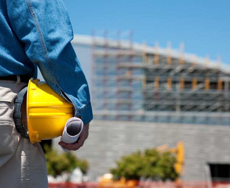 Man holding a safety gear standing in front of a construction site