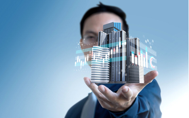 Business man holding a 3D building with graph icons