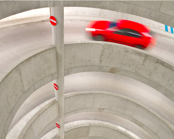 Red car driving up to the parking lot through spiral entrance ramp
